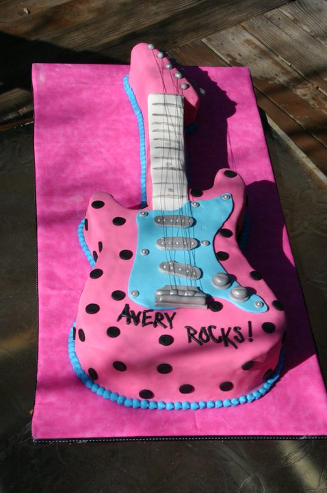 Pink sculpted guitar birthday cake with black polka dots and blue accents